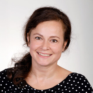 Portrait einer Frau mit dunklen, gelockten Haaren und gemustertem Oberteil.